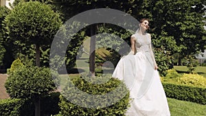 Beautiful lovely stylish bride in white wedding dress and veil walking in park and waiting for groom