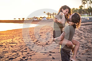 Beautiful lovely young couple on the beach during sunset having fun together, laughing. Real people emotions