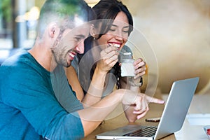 Beautiful lovely young couple using their laptop and having breakfast in the kitchen at home.