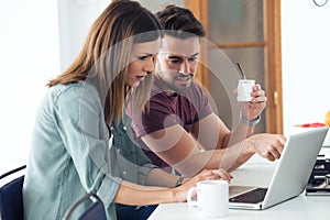 Beautiful lovely young couple using their laptop and having breakfast in the kitchen at home