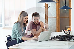 Beautiful lovely young couple using their laptop and having breakfast in the kitchen at home