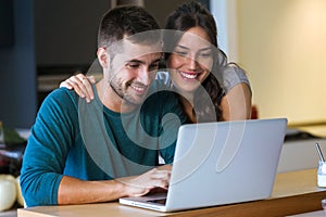 Beautiful lovely young couple using their laptop in the kitchen at home.