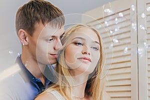 Beautiful loving couple looking out the window. Guy and girl cuddling together. Valentine`s Day. The reflection in the mirror