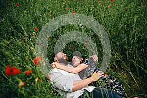 Beautiful loving couple lying on poppies field background