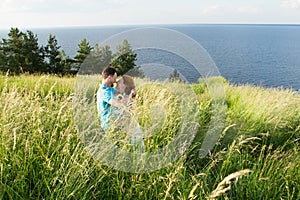 beautiful loving couple resting in summer field on big grass, caressing each other and kissing. Couple in the grass
