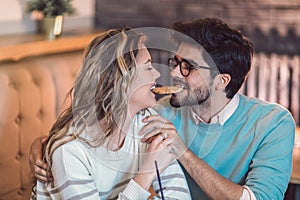 Beautiful loving couple sitting in a cafe sharing cookie.