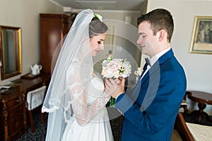 Beautiful loving wedding couple is holding flowers bouquet and kissing at luxury hotel interior background