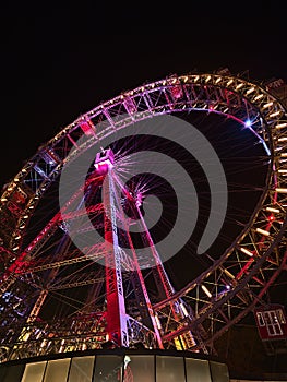 Beautiful low angle view of famous Ferris wheel with colorful rim in the dark at park Prater in Vienna, Austria.