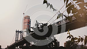 Beautiful low angle view of Manhattan Bridge in New York, trees and skyscraper under construction in background 4K.