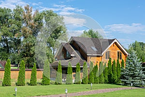 Beautiful luxury big wooden house. Timber cottage villa with with green lawn, garden and blue sky on background