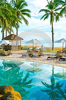 Beautiful luxury umbrella and chair around outdoor swimming pool in hotel and resort with coconut palm tree on sunset  or sunrise