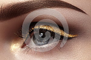 Beautiful macro shot of female eye with ceremonial makeup. Perfect shape of eyebrows, eyeliner and pretty gold line on eyelid