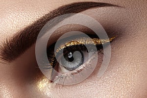 Beautiful macro shot of female eye with ceremonial makeup. Perfect shape of eyebrows, eyeliner and pretty gold line on eyelid