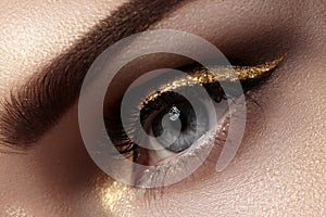 Beautiful macro shot of female eye with ceremonial makeup. Perfect shape of eyebrows, eyeliner and pretty gold line on eyelid