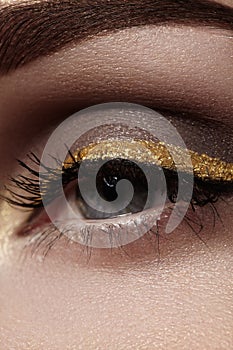 Beautiful macro shot of female eye with ceremonial makeup. Perfect shape of eyebrows, eyeliner and pretty gold line on eyelid