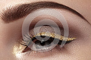 Beautiful macro shot of female eye with ceremonial makeup. Perfect shape of eyebrows, eyeliner and pretty gold line on eyelid