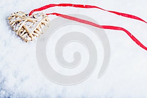 Beautiful magical vintage beige heart tied with a red ribbon on a white snow background. Winter and Christmas concept