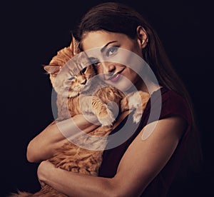 Beautiful make-up woman with brown long hair holding and tender hugging with love her red maine coon kitten. Closeup toned vintage