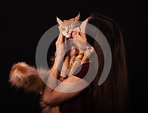 Beautiful make-up woman with brown long hair holding and tender strong kissing with love her red maine coon fun humor kitten.