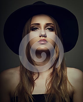 Beautiful makeup woman with long blond hair style in black hat on studio background.. Closeup