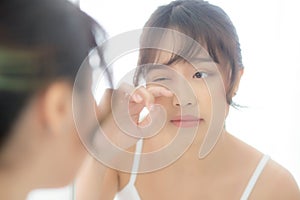 Beautiful and makeup young asian woman looking mirror aging on face and touch eye, beauty asia girl of skincare cosmetic