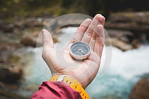 A beautiful male hand with a yellow watch strap holds a magnetic compass in a coniferous autumn forest against a