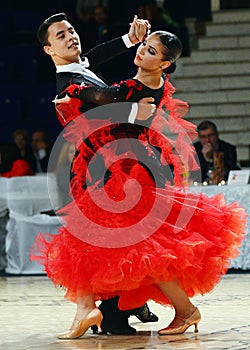 Beautiful man and woman in red dress perform smiling during dancesport competition