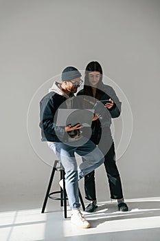 Beautiful man and woman are together in the studio against background. With laptop and tablet in hands