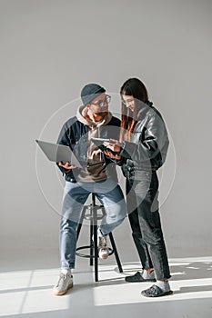 Beautiful man and woman are together in the studio against background. With laptop and tablet in hands
