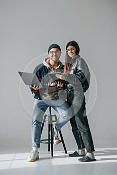 Beautiful man and woman are together in the studio against background. With laptop and tablet in hands