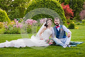 Beautiful married couple sitting on the grass in park at their wedding day