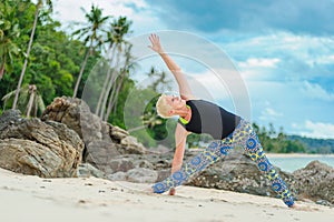 Beautiful mature aged woman doing yoga on a desert tropical beach