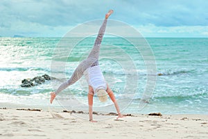 Beautiful mature aged woman doing yoga on a desert tropical beach