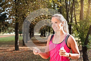 Beautiful mature blonde woman running at the park on a sunny day. Female runner listening to music while jogging