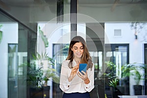 Beautiful mature business woman executive using smartphone walking in office.