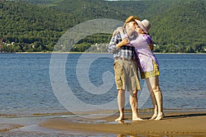 Beautiful mature sportive couple walks along the sandy river bank on a summer sunny day with mountains