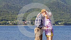 Mature sportive couple walks along the sandy river bank on a summer sunny day with mountains in the background