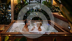 Beautiful mature couple relaxing in hot tub, drinking champagne, enjoying romantic wellness weekend in spa. Concept