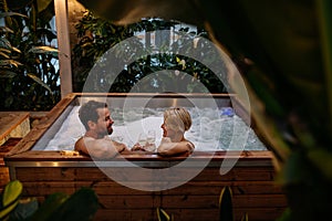 Beautiful mature couple relaxing in hot tub, drinking champagne, enjoying romantic wellness weekend in spa. Concept