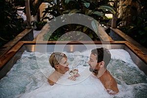 Beautiful mature couple relaxing in hot tub, drinking champagne, enjoying romantic wellness weekend in spa. Concept