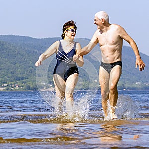 Beautiful mature couple runs on the water along the wild beach