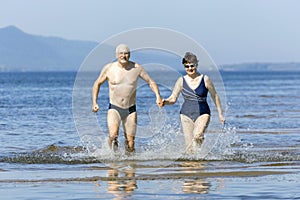 Beautiful mature couple runs on the water along the wild beach