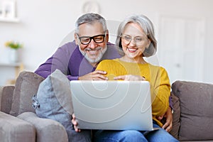 Beautiful mature family couple looking at laptop with smile on face while spending time together