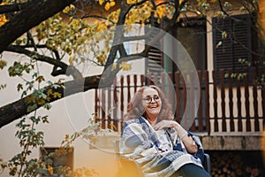 Beautiful mature happy senior smiling woman relaxing while sitting in an armchair in the autumn garden of her country