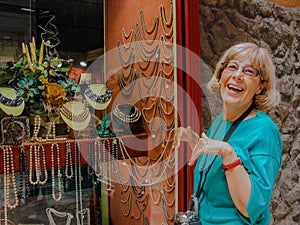 Beautiful mature happy tourist woman stays smiling at jewelry show-window