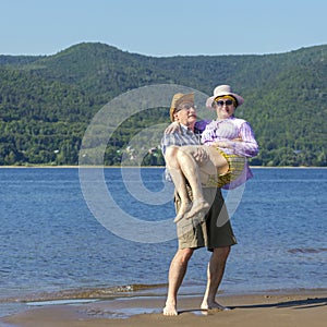 Beautiful mature man holding his beloved woman in his arms on a sandy beach on a summer sunny day against a background