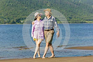 Beautiful mature sportive couple walks along the sandy river bank on a summer sunny day with mountains