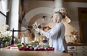 Beautiful mature woman arranging bouquet of roses in a vase, a hobby and relaxation. Older woman living alone, enjoying