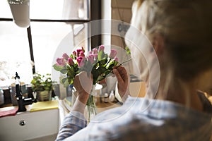 Beautiful mature woman arranging bouquet of roses in a vase, a hobby and relaxation. Older woman living alone, enjoying