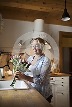 Beautiful mature woman arranging bouquet of roses in a vase, a hobby and relaxation. Older woman living alone, enjoying